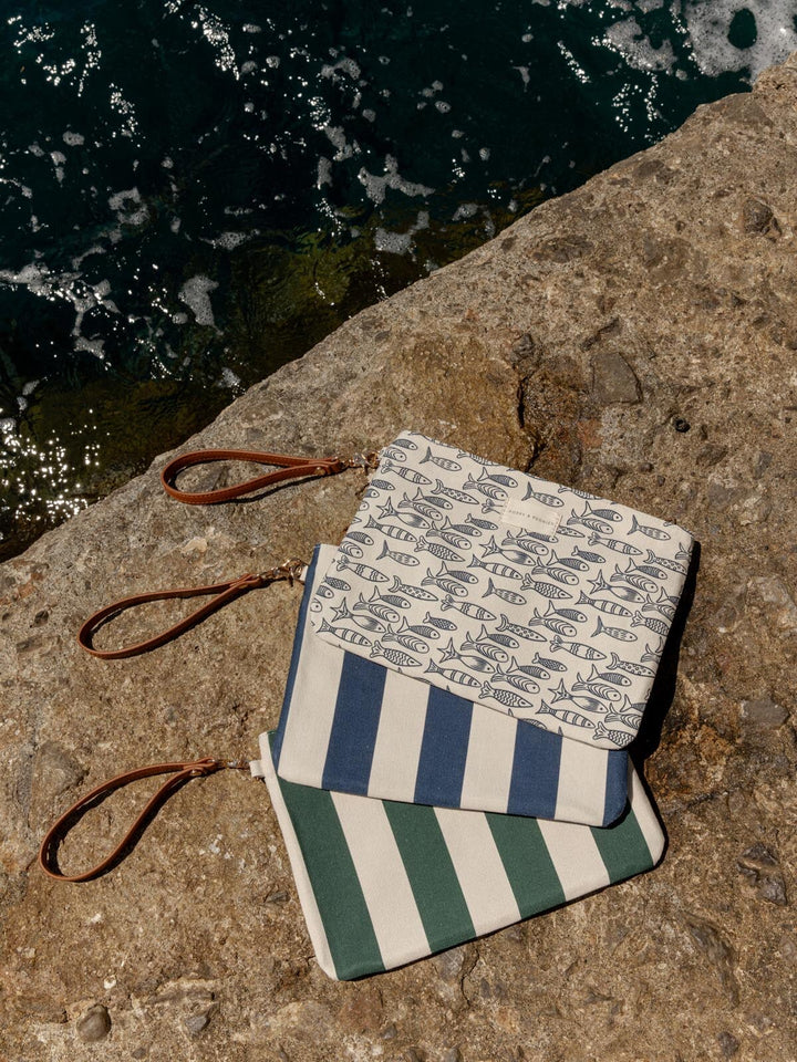 Three wet bags with a sardine pattern and stripes on a stone surface near water.