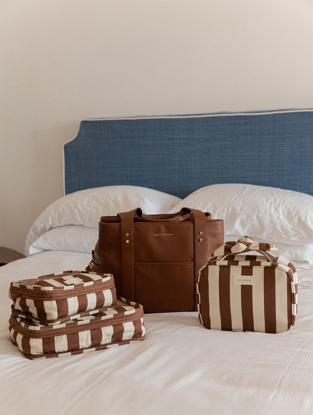 Brown and beige striped luggage set on a bed with a blue headboard.