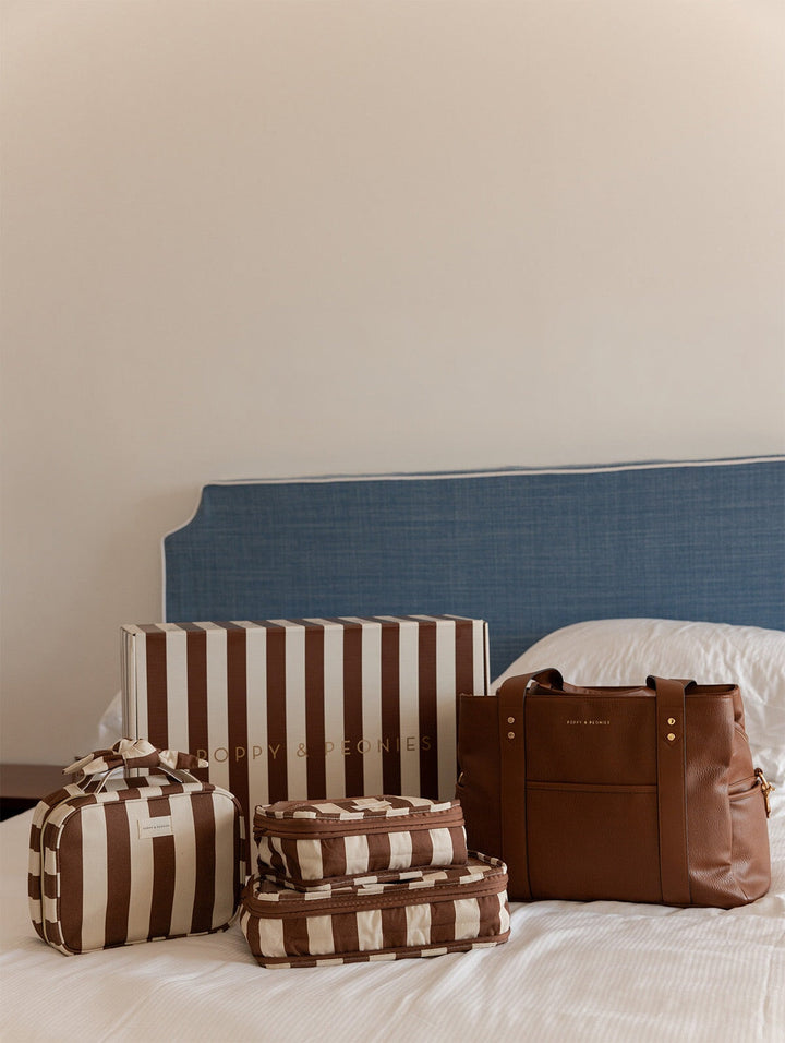 Set of brown and white striped bags and a brown vegan leather handbag on a bed with a blue headboard.