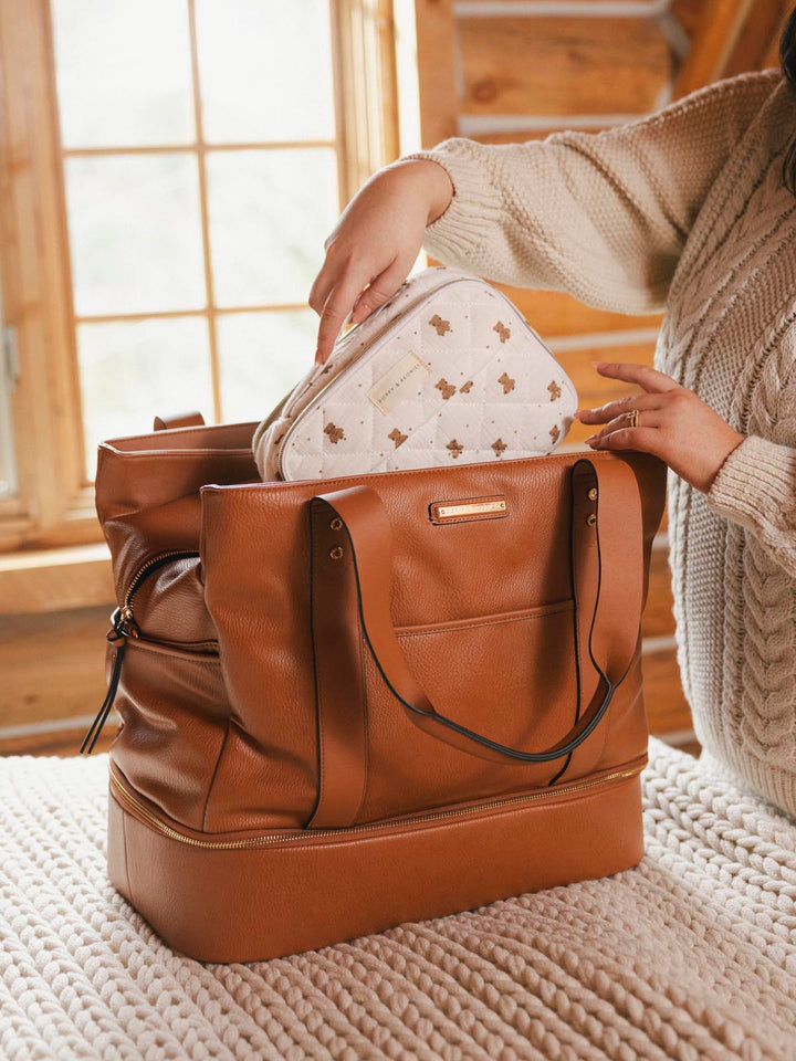 Small white makeup bag being placed inside a vegan leather travel bag