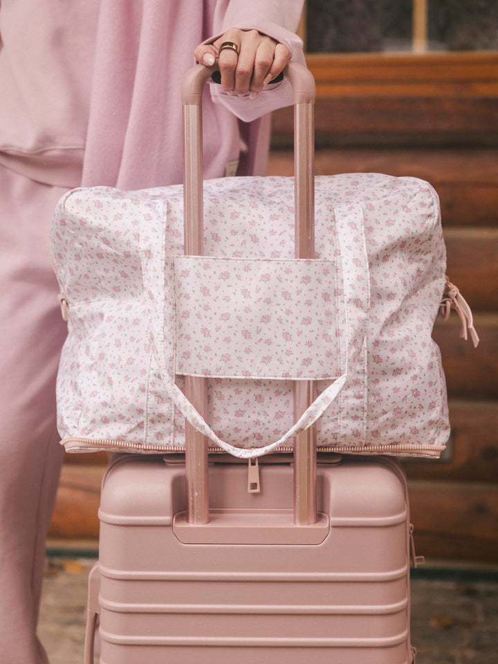 Floral-patterned duffel bag with a trolley sleeve on a suitcase