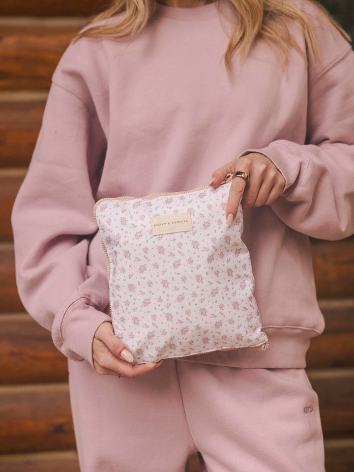 Person holding a floral-patterned pouch containing a packable duffel bag