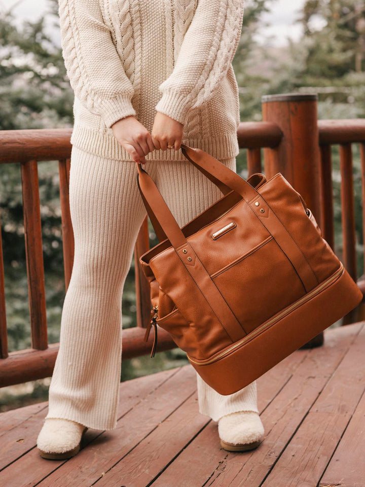 Person holding a brown vegan leather bag on a wooden deck with a blurred natural background