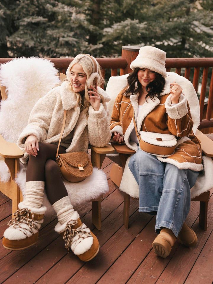 Two women in winter clothing sitting on a wooden deck with matching Poppy and Peonies faux fur bags.