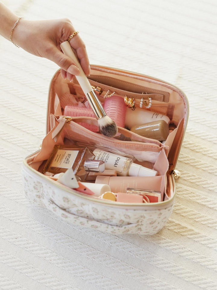 Open makeup case with various cosmetic items and a hand holding a brush
