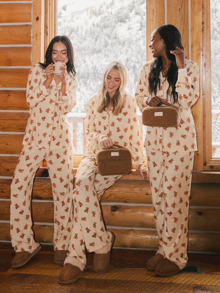 Three women in matching pajama sets holding faux fur cosmetic bags.