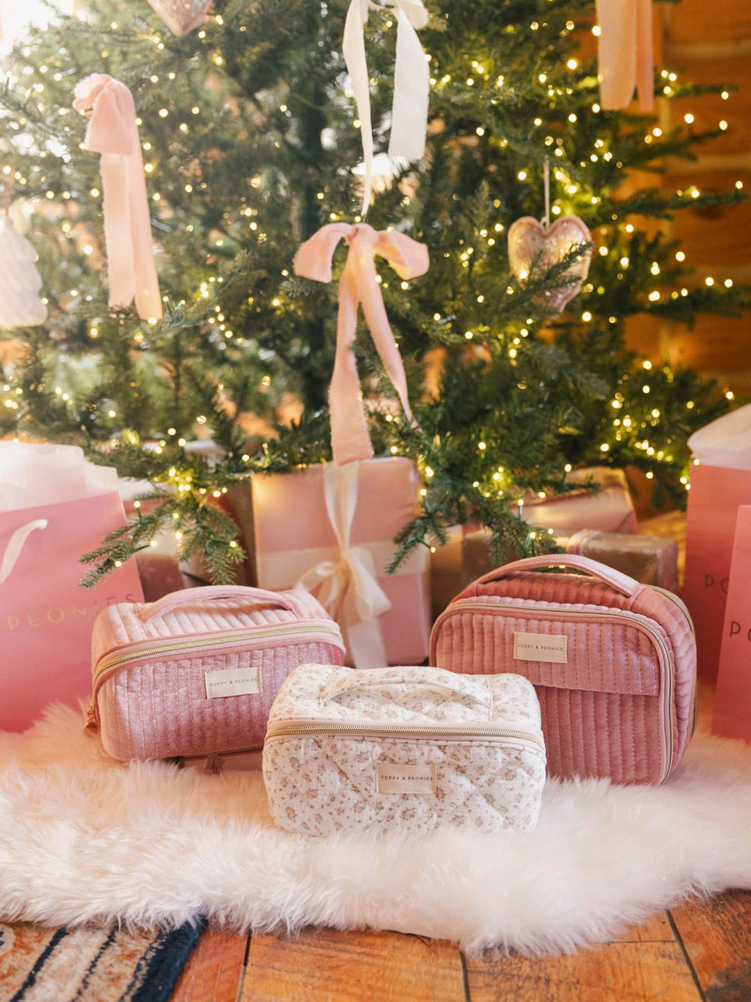 Three cosmetic cases and pink gift bags under a Christmas tree