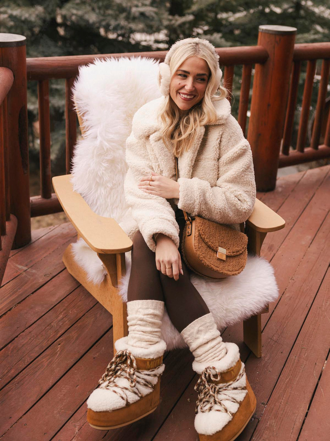 Woman in a fluffy white coat and handbag sitting on a wooden chair outdoors.