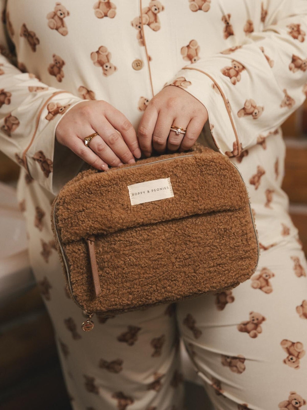 Person holding a brown faux fur cosmetic bag, wearing pajamas with teddy bear pattern.