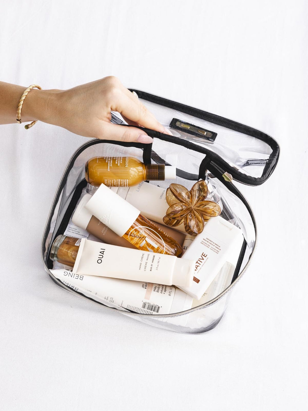 Clear travel pouch with skincare products inside, held by a hand on a white background