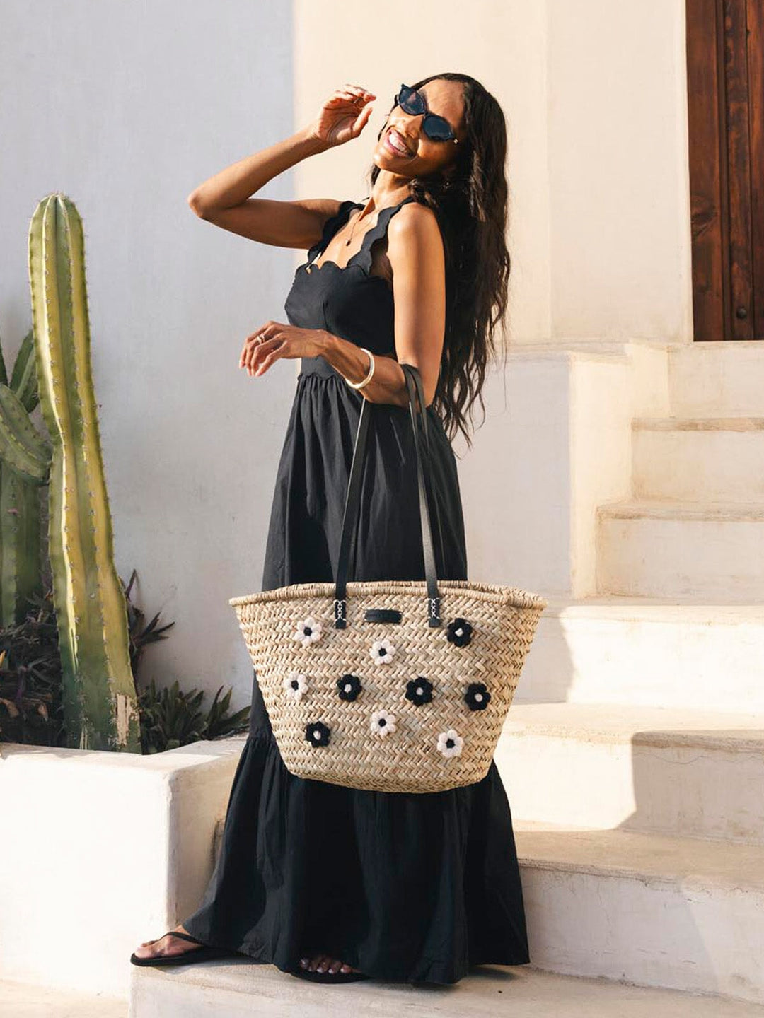 Woman in a black dress holding a straw bag with floral adornments