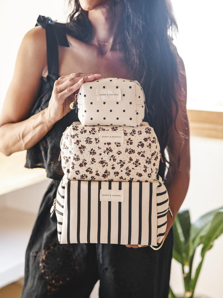 Woman holding a stack of three patterned cosmetic bags 