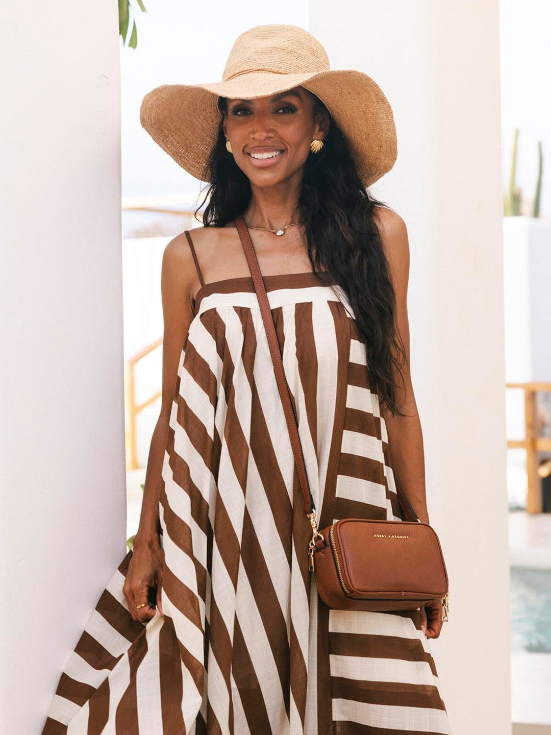 Woman wearing a brown and white striped dress with a wide-brimmed hat and carrying a matching handbag.