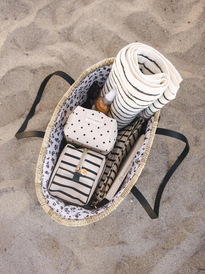 Straw bag packed with cosmetic bags and a towel on a sandy surface