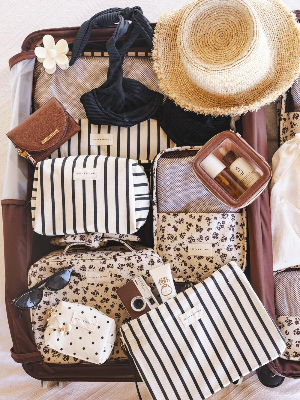 Open suitcase with various travel items including a hat, sunglasses, and Poppy and Peonies bags.