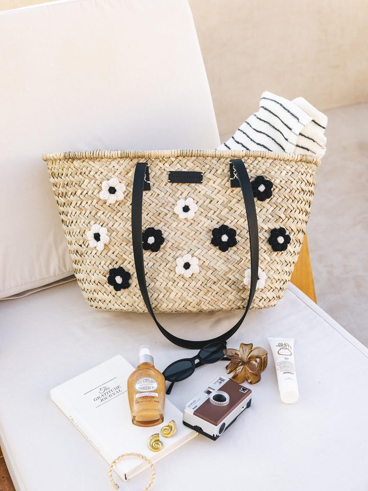 Straw bag with floral adornments on a chair with accessories around