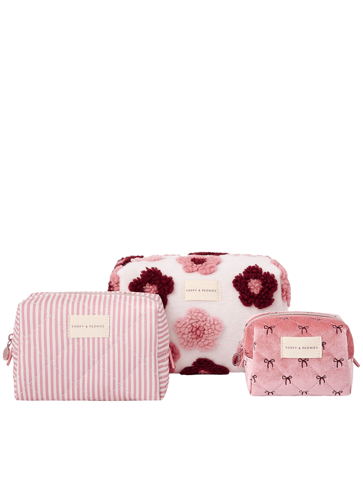 Poppy and Peonies Cosmetic Trio Floral featuring three coordinating cosmetic pouches in different sizes, including a large cream pouch with pink and berry floral patterns, a medium pink and white striped pouch, and a small pink pouch with delicate black bow patterns, accented with gold-tone hardware and logo plates.