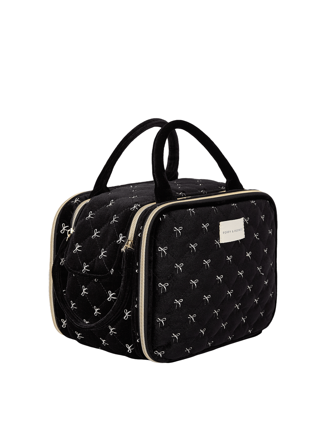 Poppy and Peonies The Routine Cosmetic Black Velvet displayed at a three-quarter angle, highlighting its structured rectangular shape, soft black velvet exterior with white bow patterns, dual black top handles, zip-around closure, and spacious side profile.