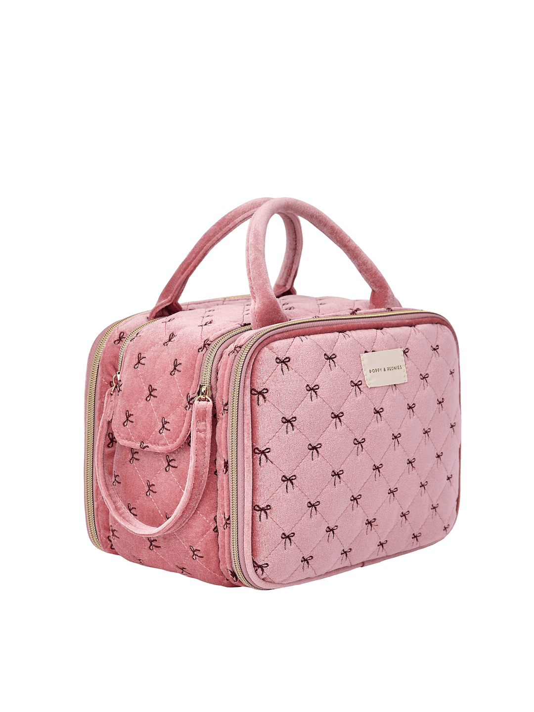 Poppy and Peonies The Routine Cosmetic Pink Velvet displayed at a three-quarter angle, highlighting its structured rectangular shape, soft pink velvet exterior with black bow patterns, dual pink top handles, zip-around closure, and spacious side profile.