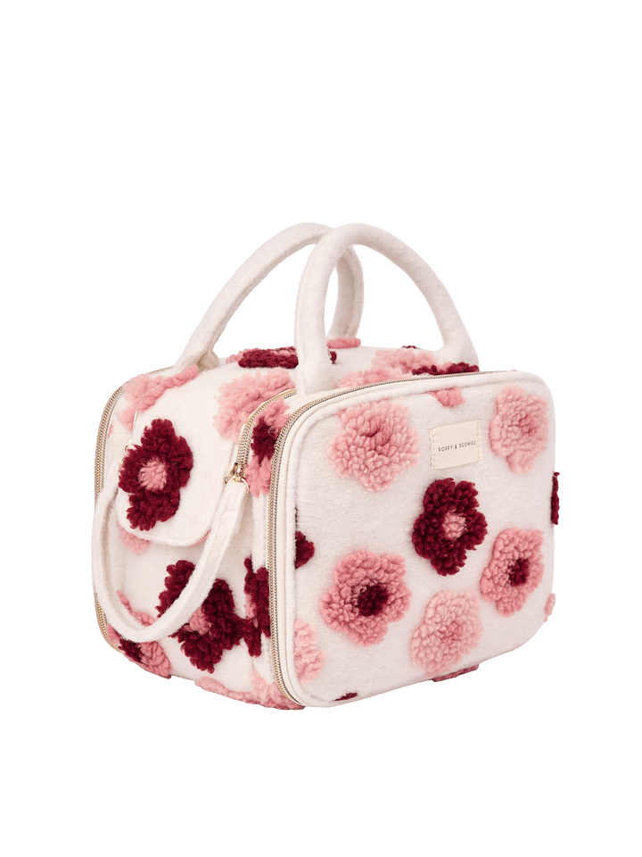 Poppy and Peonies The Routine Cosmetic Floral displayed at a three-quarter angle, highlighting its structured rectangular shape, soft cream-colored exterior with raised pink and berry floral patterns, dual cream top handles, zip-around closure, and spacious side profile.