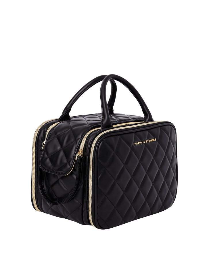 Poppy and Peonies The Routine Cosmetic Black displayed at a three-quarter angle, highlighting its structured rectangular shape, black diamond-quilted exterior, dual black top handles, gold-tone zip-around closure, and spacious side profile.