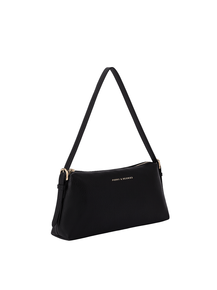Poppy & Peonies The Soho Shoulder Bag in Black, shown from a three-quarter angle highlighting its slim profile, adjustable shoulder strap with buckle details, gold-tone hardware, and pebbled texture.