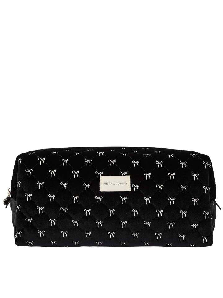 Poppy and Peonies The Mane Character Case Black Velvet featuring a structured rectangular silhouette, soft black velvet exterior with delicate white bow patterns, rounded edges, zippered top closure, and rectangular gold Poppy and Peonies logo plate on the front.