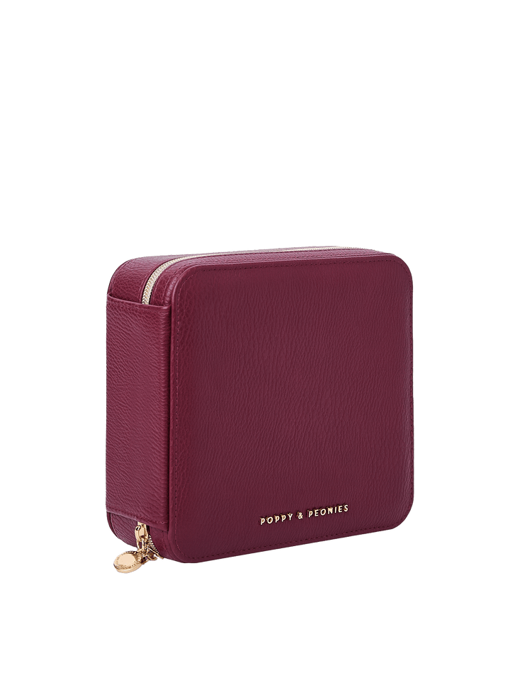 Poppy and Peonies The Out of Office Case Berry displayed at a three-quarter angle, highlighting its structured square shape, textured berry exterior, gold-tone zip-around closure, round zipper pull, and subtle Poppy and Peonies logo near the bottom.
