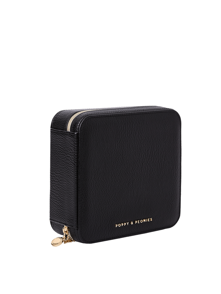 Poppy and Peonies The Out of Office Case Black displayed at a three-quarter angle, highlighting its structured square shape, textured black exterior, gold-tone zip-around closure, round zipper pull, and subtle Poppy and Peonies logo near the bottom.