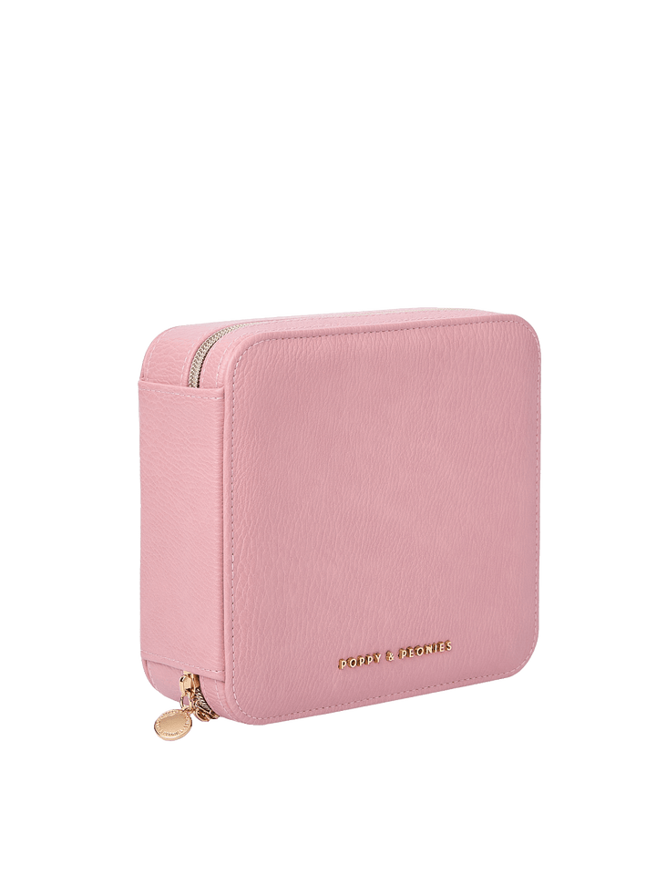 Poppy and Peonies The Out of Office Case Rosé displayed at a three-quarter angle, highlighting its structured square shape, textured soft pink exterior, gold-tone zip-around closure, round zipper pull, and subtle Poppy and Peonies logo near the bottom.
