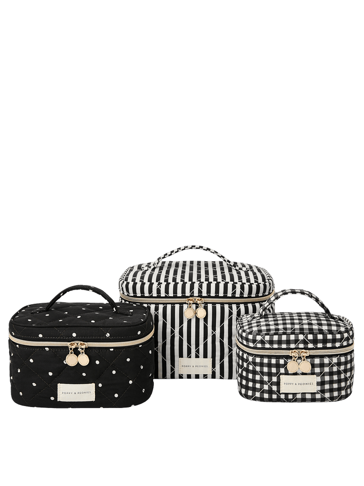 Poppy and Peonies Travel Trio Black Stripe featuring three coordinating travel cases in different sizes, including a large black and white striped case, a medium black case with delicate white bow patterns, and a small black and white striped case, all with top carrying handles, gold-tone zipper closures, and rectangular logo plates.