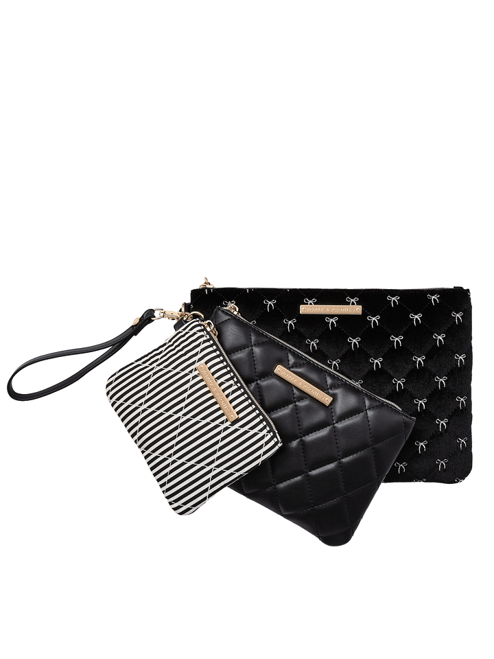 Poppy and Peonies The Clutch Trio Black Velvet displayed as a coordinated set of three overlapping pouches, showcasing the large black velvet clutch with white bow patterns, medium black diamond-quilted pouch, and small black and white striped pouch with gold-tone hardware and wristlet straps.