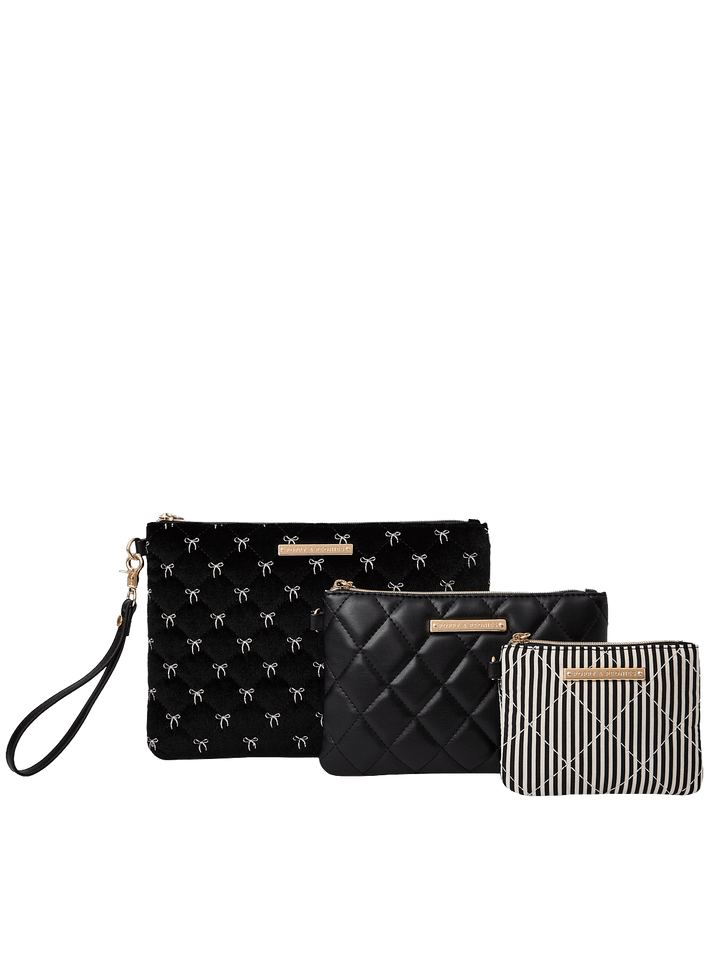 Poppy and Peonies The Clutch Trio Black Velvet featuring three coordinating pouches in different sizes, including a large black velvet clutch with delicate white bow patterns, a medium black diamond-quilted pouch, and a small black and white striped pouch, accented with gold-tone hardware.