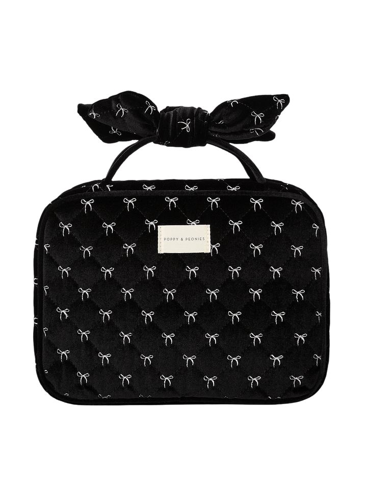 Poppy and Peonies Hook Me Up Cosmetic Case Black Velvet featuring a structured rectangular silhouette, soft black velvet exterior with delicate white bow patterns, decorative bow-shaped top handle, zip-around closure, and rectangular gold Poppy and Peonies logo plate on the front.