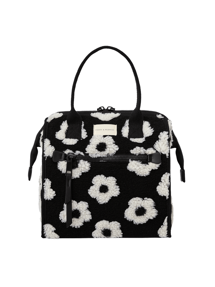 Poppy and Peonies The Lunch Bag Black Floral displayed from the front, showcasing its black exterior with white floral patterns, dual top handles, structured rectangular silhouette, and front logo plate.