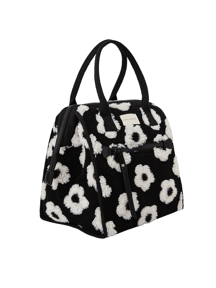 Poppy and Peonies The Lunch Bag Black Floral displayed at a three-quarter angle, highlighting its structured silhouette, black exterior with white floral patterns, dual top handles, and spacious side profile.
