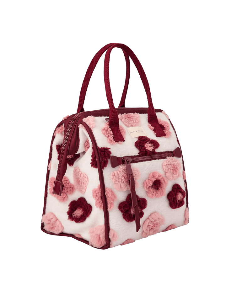 Poppy and Peonies The Lunch Bag Berry Floral displayed at a three-quarter angle, highlighting its structured silhouette, cream-colored exterior with pink and berry floral patterns, contrasting berry trim, dual top handles, and spacious side profile.