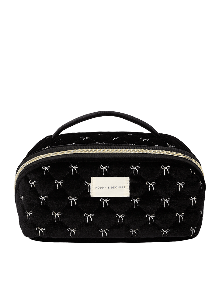 Poppy and Peonies Open and Glow Cosmetic Case Black Velvet featuring a structured rectangular silhouette, soft black velvet exterior with delicate white bow patterns, top carrying handle, gold-tone zip-around closure, front zippered pocket, and rectangular gold Poppy and Peonies logo plate.