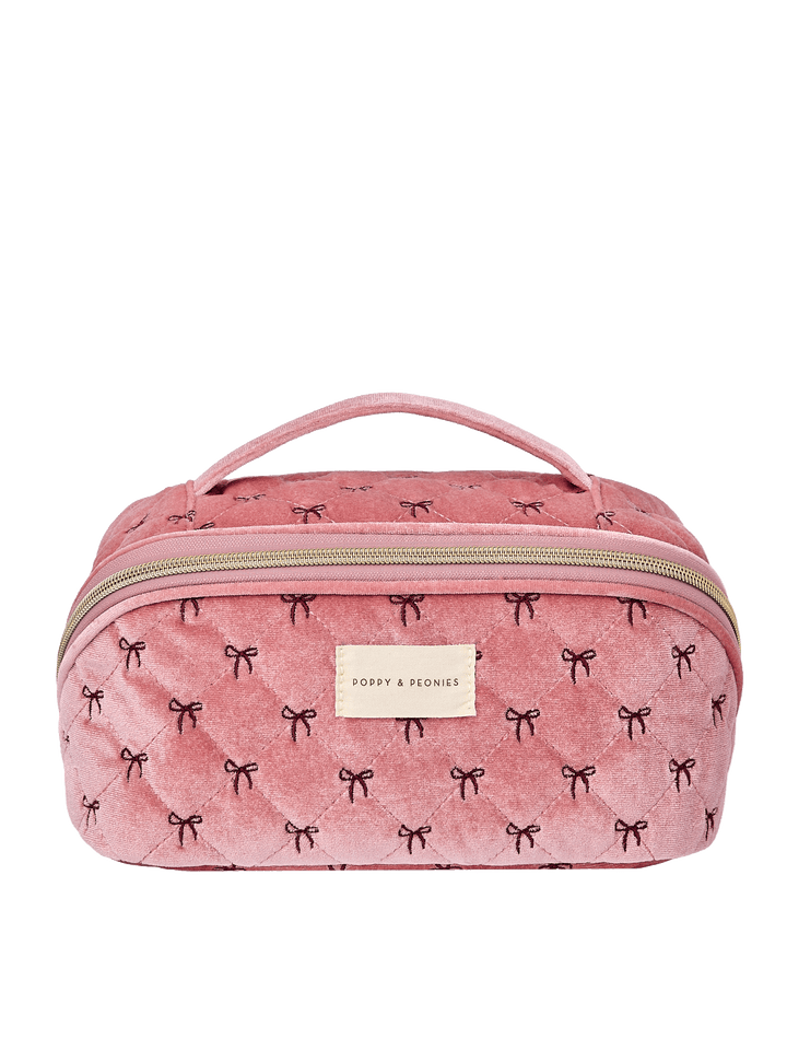 Poppy and Peonies Open and Glow Cosmetic Case Pink Velvet featuring a structured rectangular silhouette, soft pink velvet exterior with delicate black bow patterns, top carrying handle, gold-tone zip-around closure, front zippered pocket, and rectangular gold Poppy and Peonies logo plate.