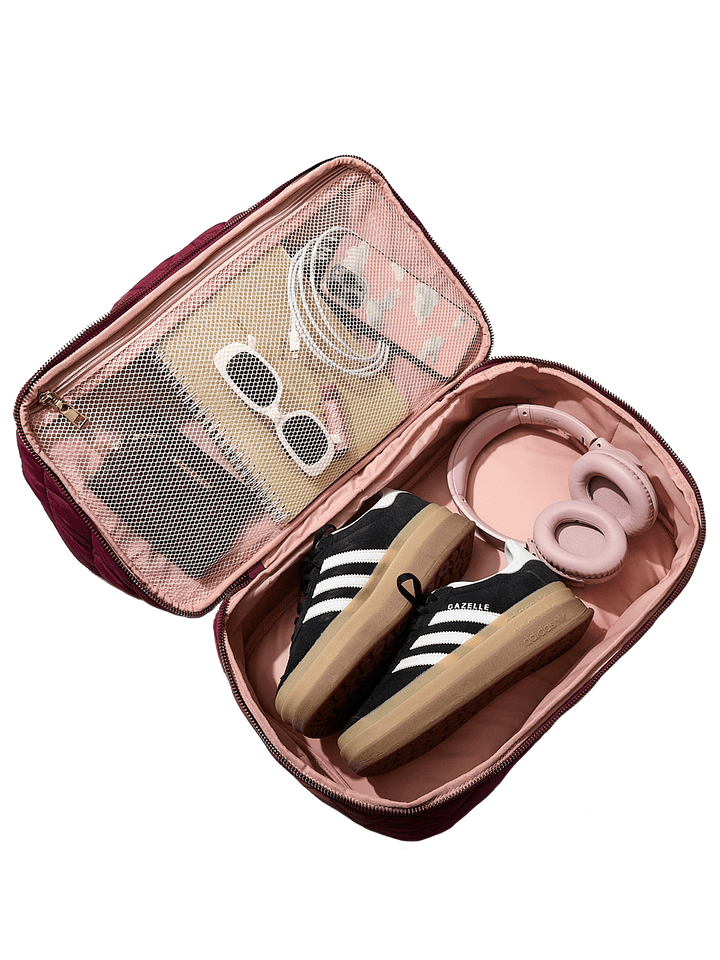 Berry coloured travel bag with a sneaker, sunglasses, and other items on a transparent background