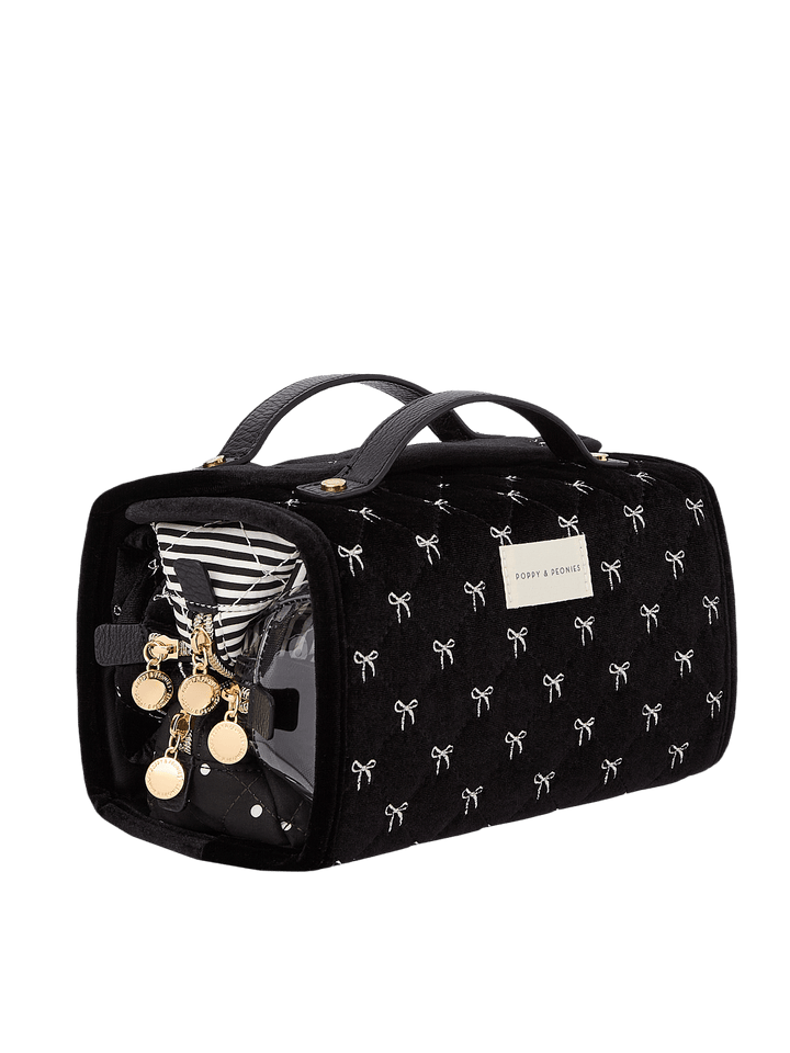 Poppy and Peonies The Glam Squad Cosmetic Case Black Velvet displayed at a three-quarter angle with its side compartment open, highlighting its black velvet exterior with white bow patterns, structured rectangular shape, dual top handles, and organized interior filled with beauty essentials.