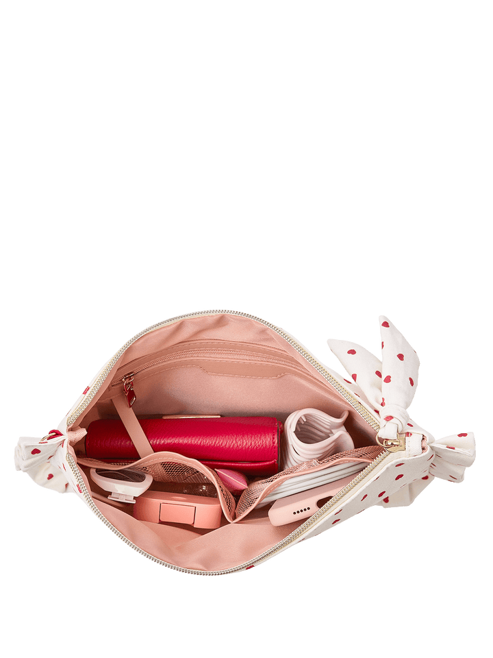 White clutch with red heart pattern containing a wallet and other items