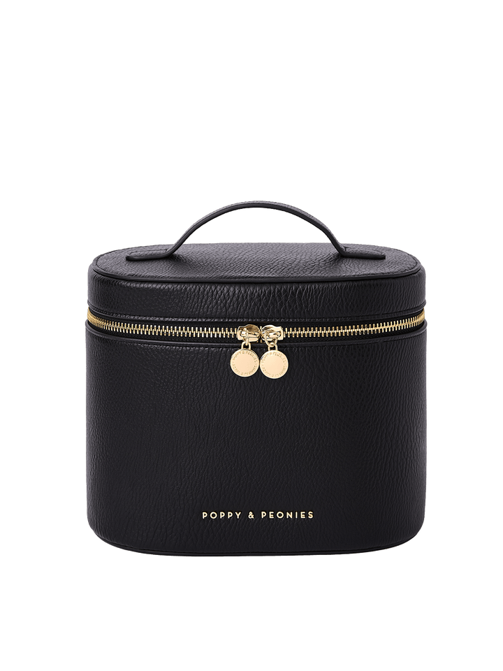 Poppy and Peonies The Vanity Case Black featuring a structured rounded rectangular silhouette, textured black exterior, top carrying handle, gold-tone zip-around closure with double round zipper pulls, and gold Poppy and Peonies logo near the bottom.
