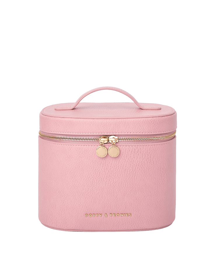 Poppy and Peonies The Vanity Case Rosé featuring a structured rounded rectangular silhouette, soft pink textured exterior, top carrying handle, gold-tone zip-around closure with double round zipper pulls, and gold Poppy and Peonies logo near the bottom.