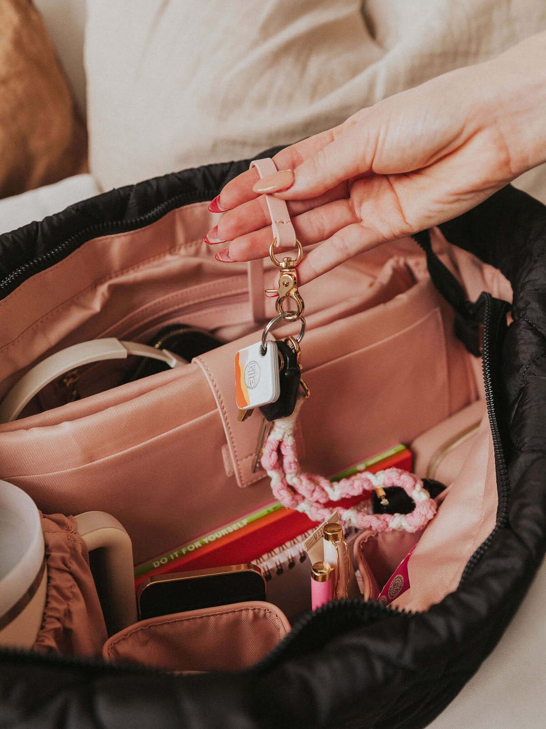 Person holding a keychain over an open quilted tote bag with various items inside.