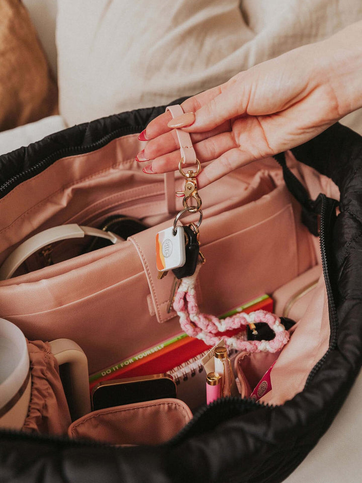 Person holding a keychain over an open quilted tote bag with various items inside.