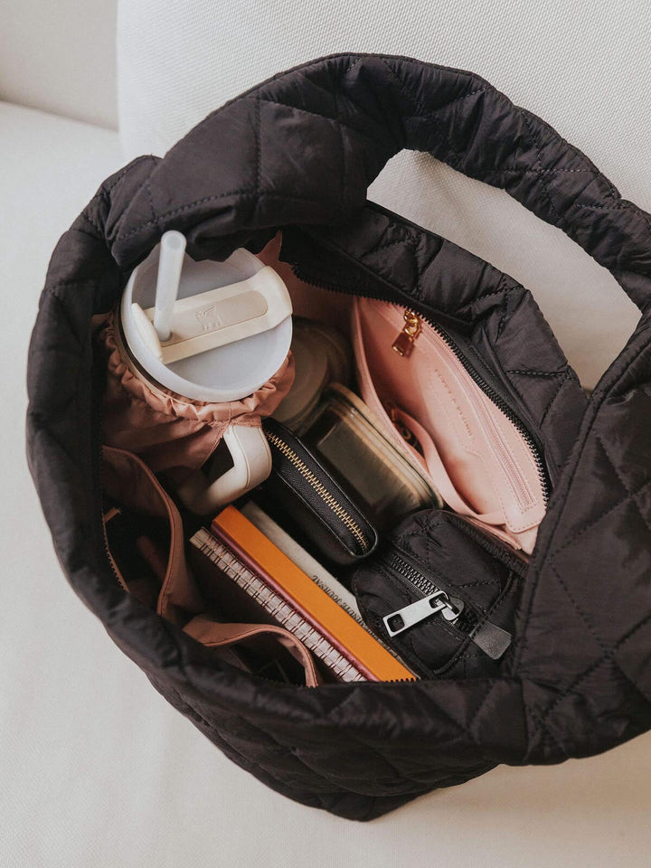 Black quilted bag with various items including a water bottle and a notebook on a light background