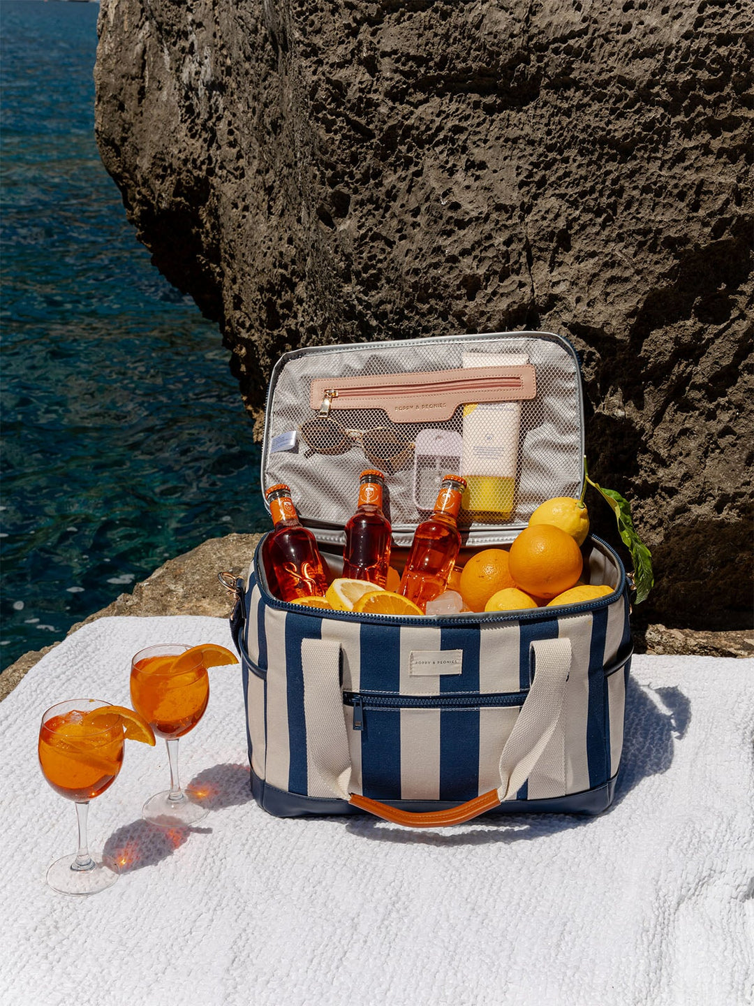 Open blue and white striped cooler bag with drinks and snacks by a rocky coastline