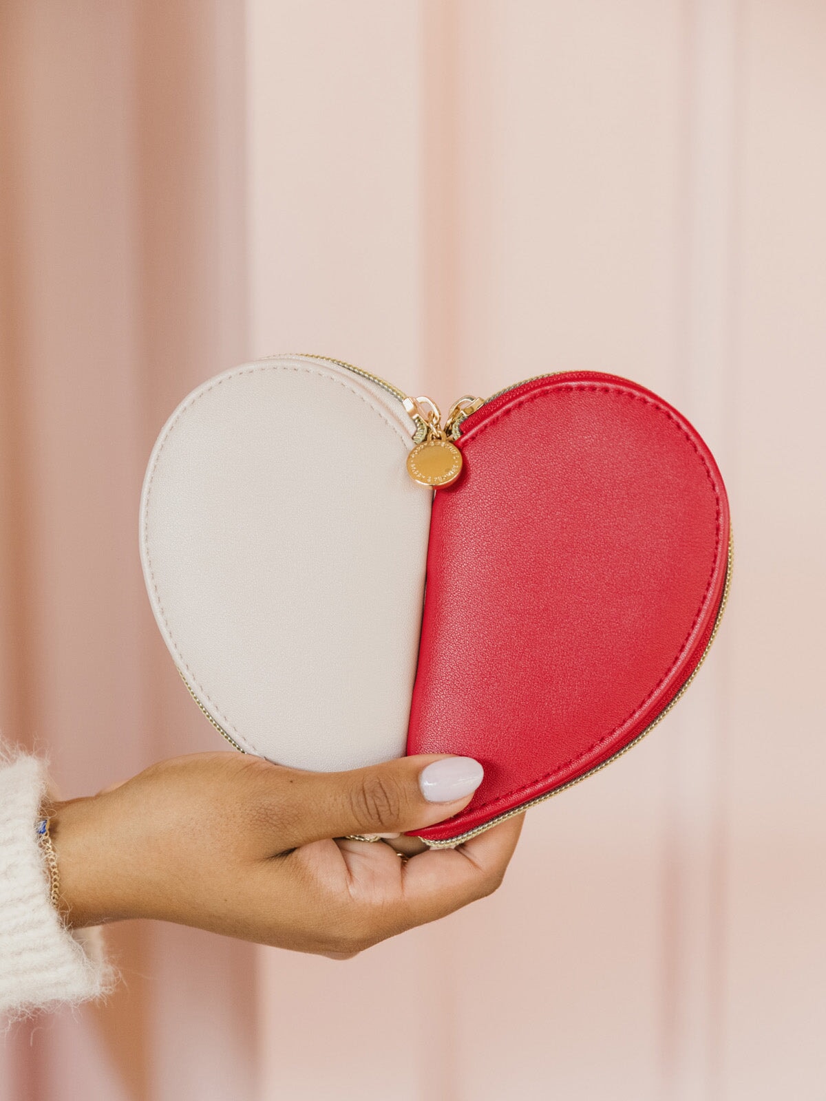 Heart-shaped coin purse held by a hand against a soft pink background