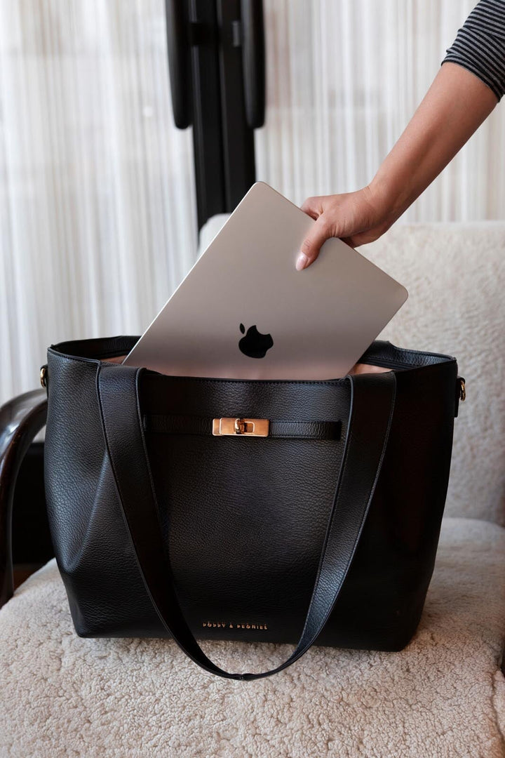 Person placing a silver laptop into a black vegan leather tote bag